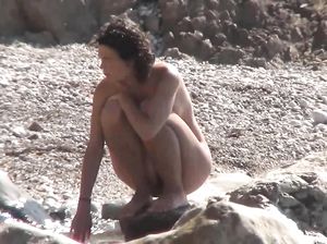 Брюнетка отдыхает на каменистом пляже, не заметив слежки